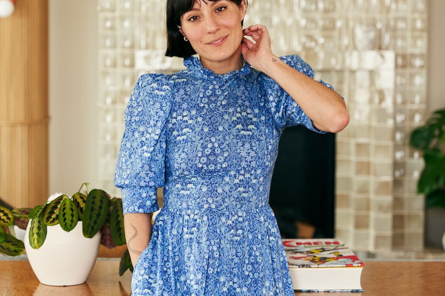 A woman with short dark hair wearing a blue and white floral print dress standing in front of a wood and marble table.