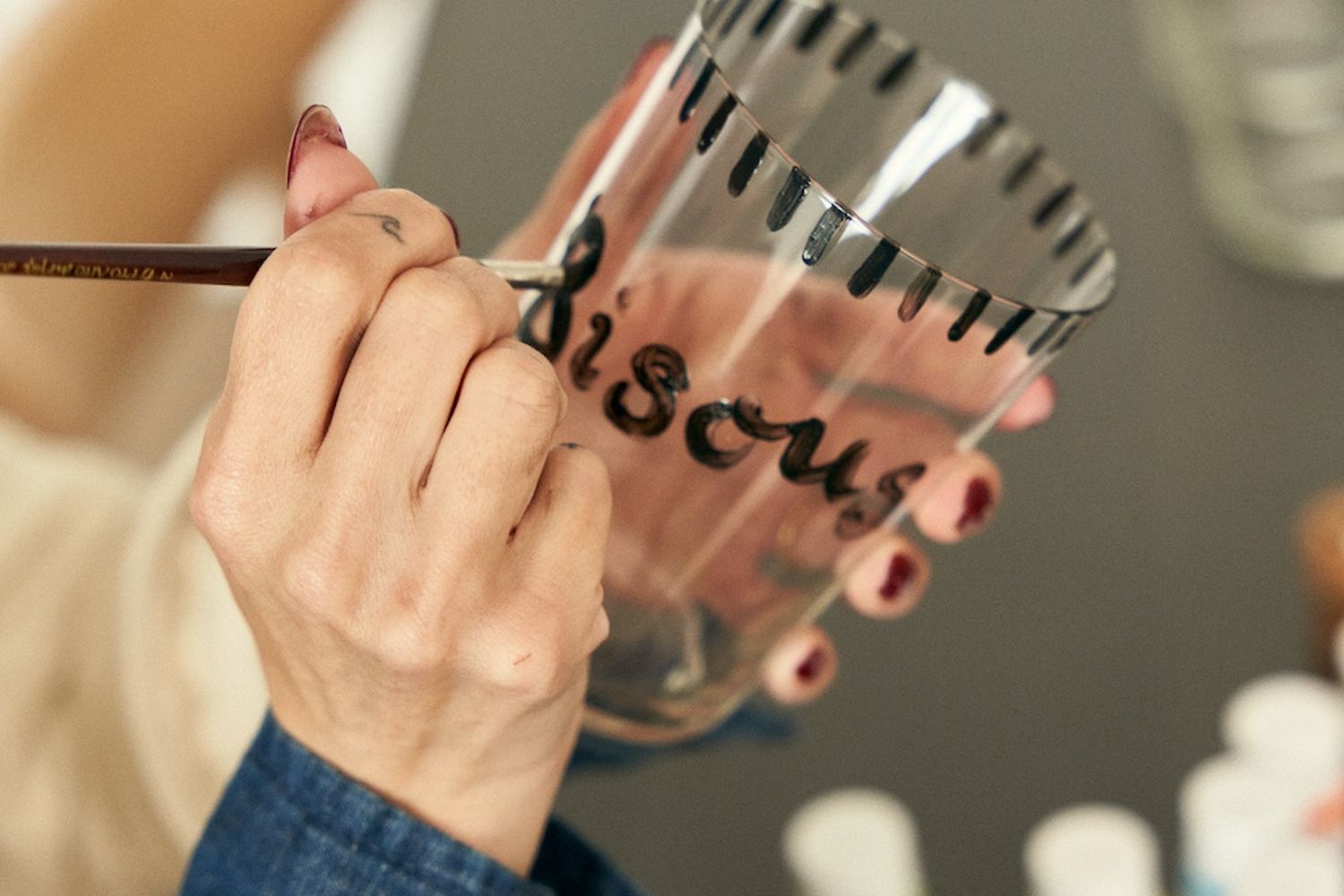 A woman is painting black letters on a drinking glass.