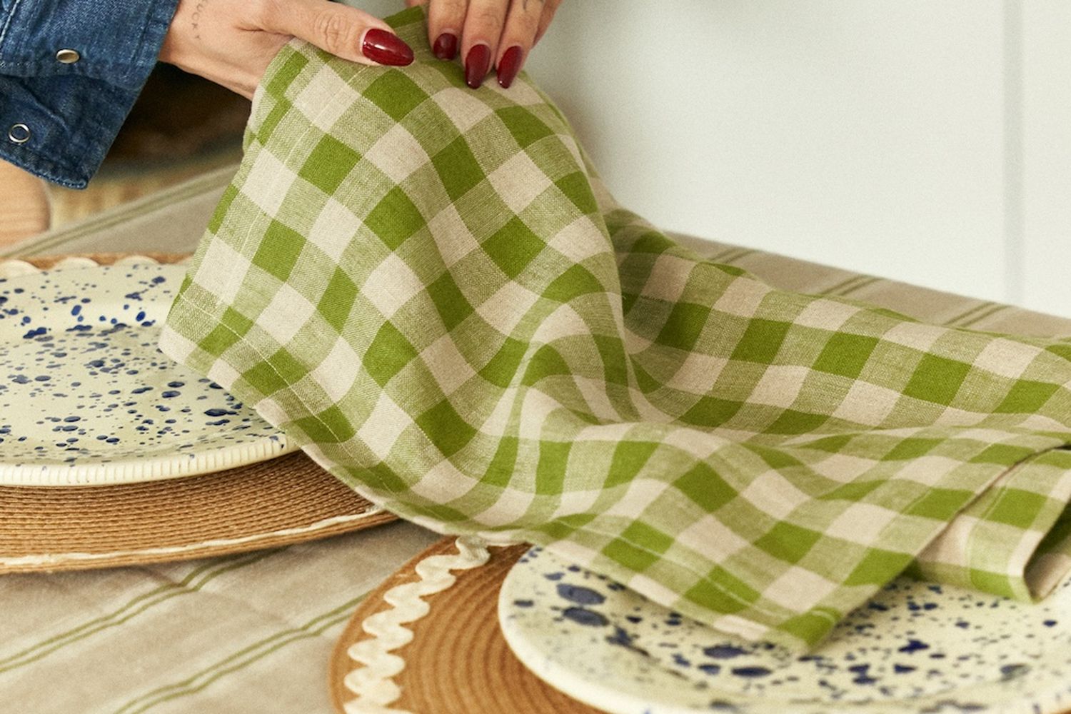 A woman is folding green gingham napkins at a table.