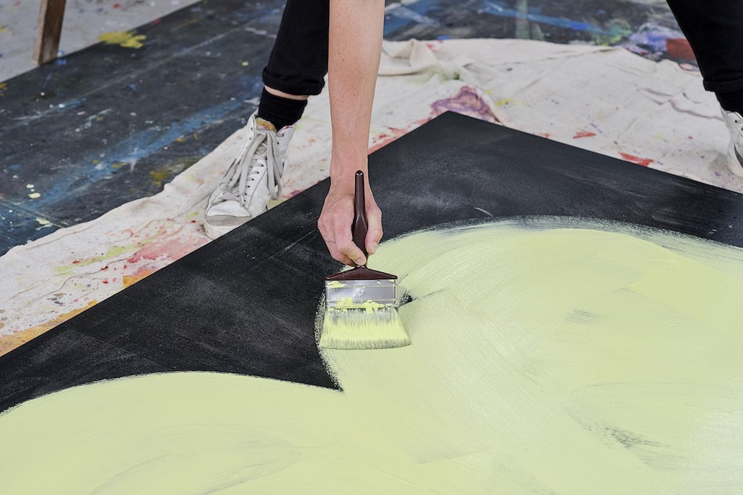 A person is painting a large, yellow and black abstract design on a canvas. The person is using a paintbrush to apply the design. [G]