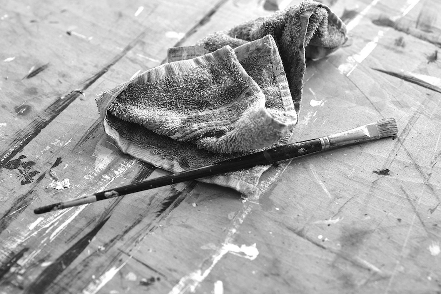 black and white photo of a painting brush and a towel on a wooden surface. [G]