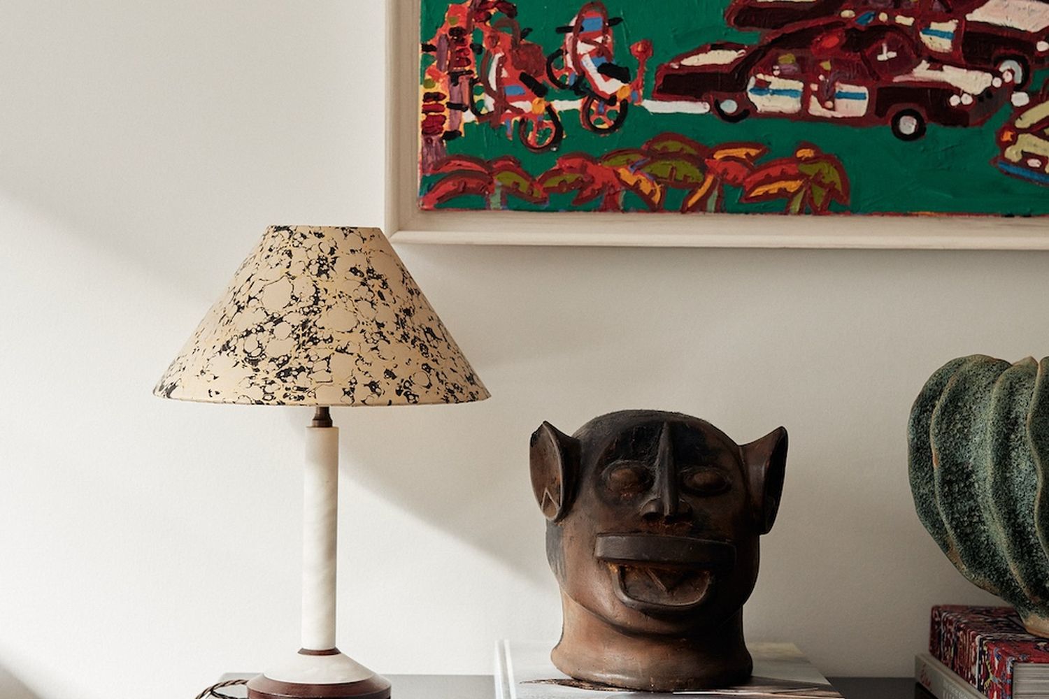 A lamp with a black and white shade sits next to a sculpture of a monkey type figure.