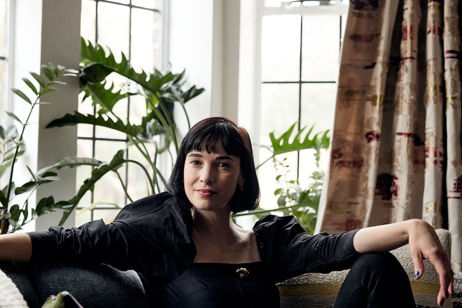 A woman is leaning back on a sofa in front of a window.