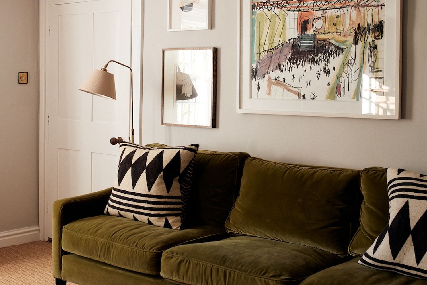 A cozy living room with a green couch adorned with black and white geometric pillows, a lamp with a beige shade, and a book on the floor. [G]