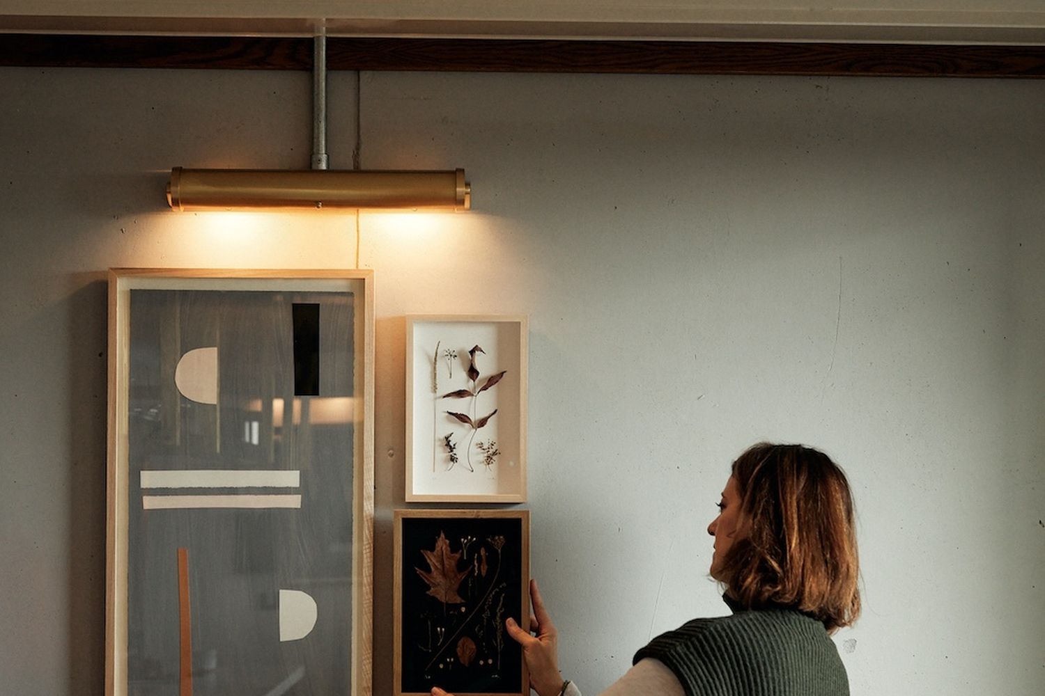 A woman in a green sweater is pointing at a framed picture on a wall. [G]