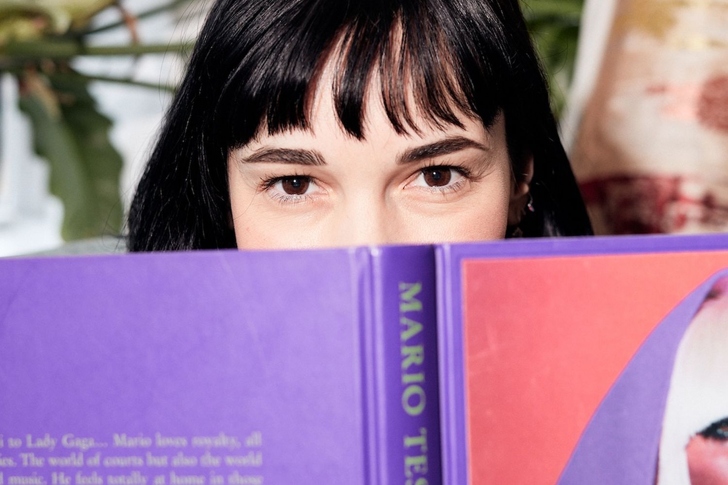 A woman peeks over a book with a purple cover.