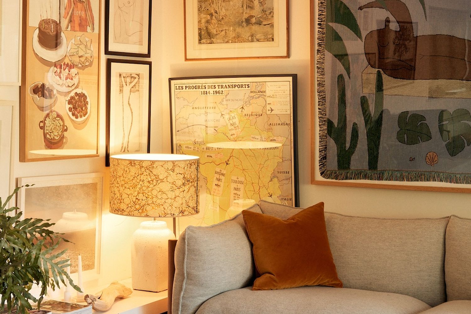 A cozy living room with a large sofa, a lamp, and various artwork. [G]