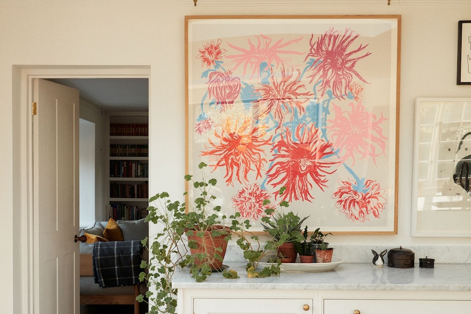 A room with a white cabinet, a large pink and red painting, and a potted plant. [G]