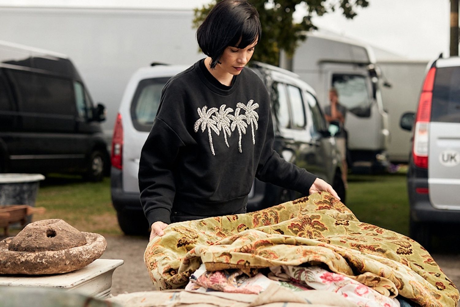 A woman is looking at rugs on a table.