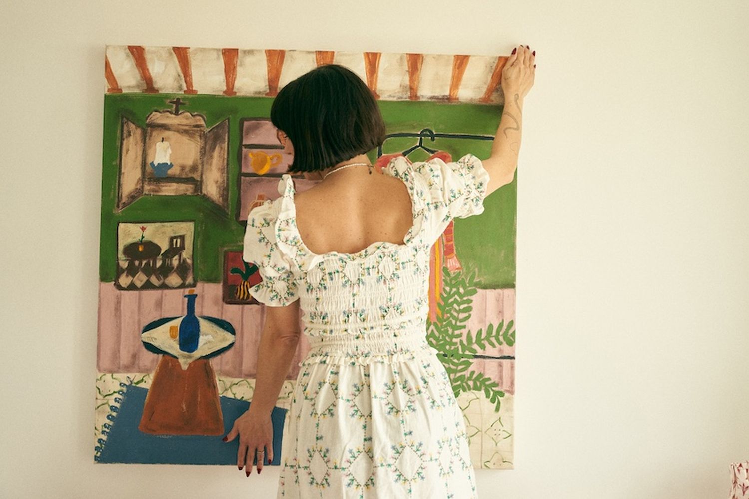 A woman hanging a large print on a bedroom wall.
