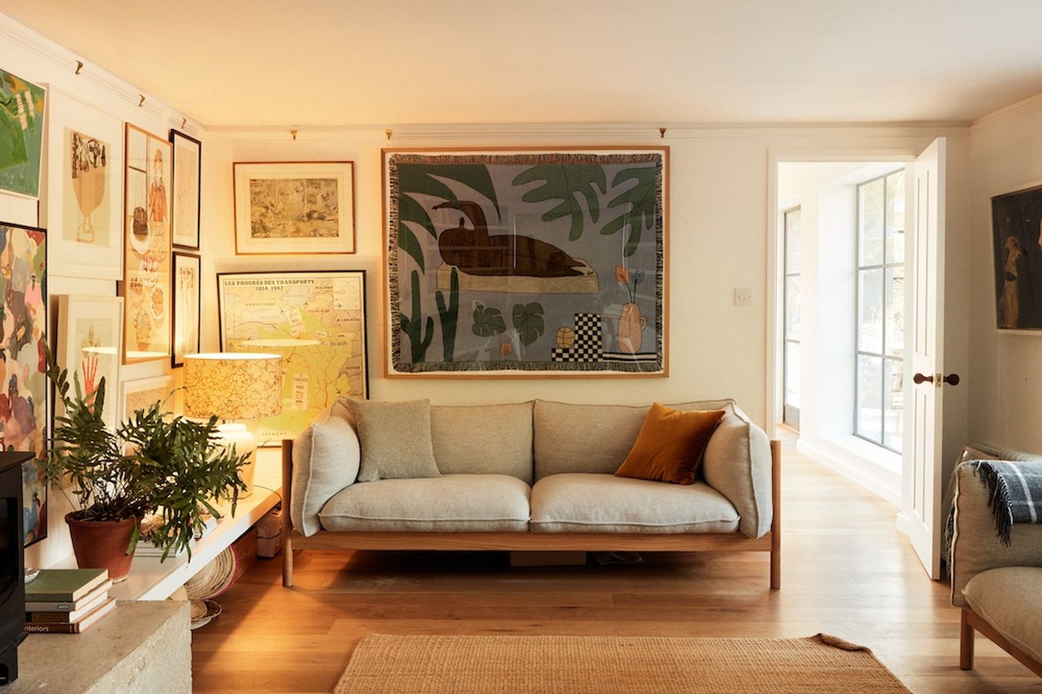A cozy living room with a large beige sofa adorned with multiple pillows, a wooden coffee table, and a map on the wall. [G]
