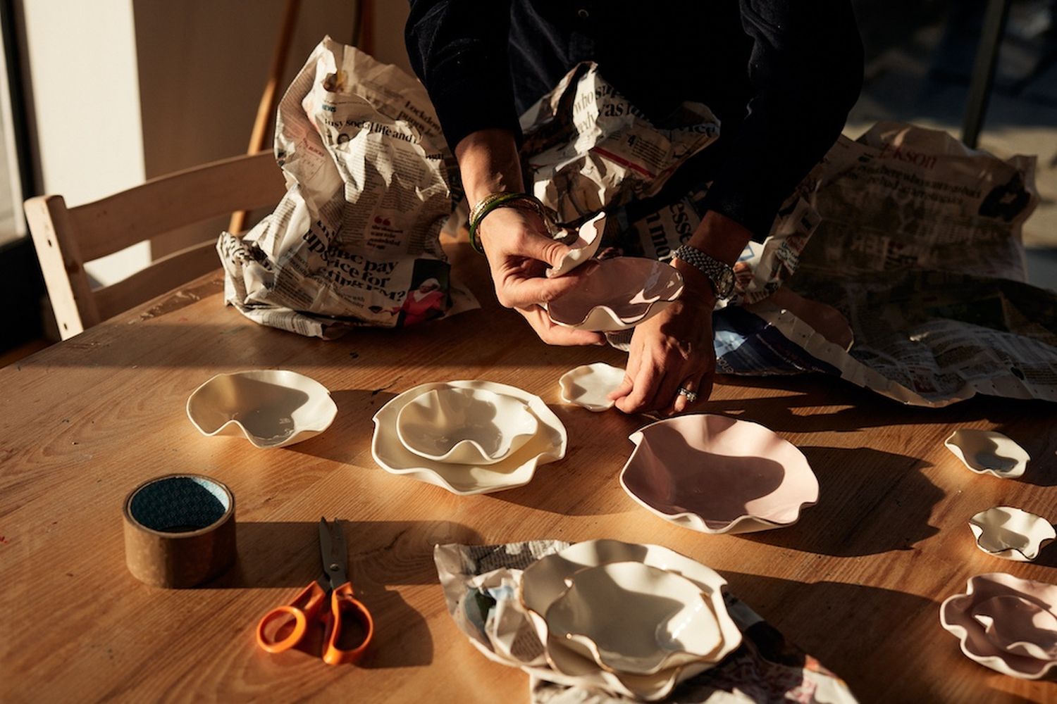 A person is crafting pottery at a wooden table. They are using scissors and a piece of paper to shape and shape their pottery. [G]