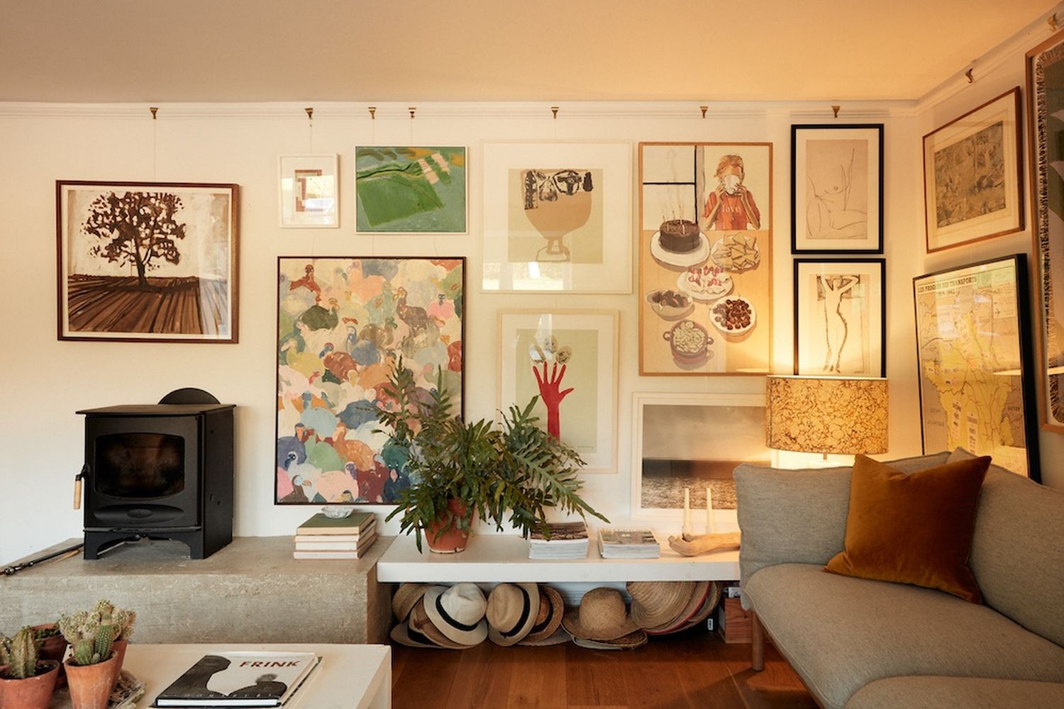 A cozy living room with a fireplace, a coffee table, and various artwork. [G]