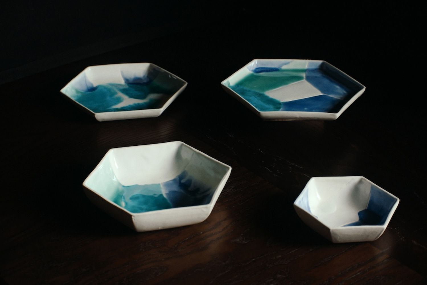 4 blue-green and white bowls of various sizes on a dark wooden table.