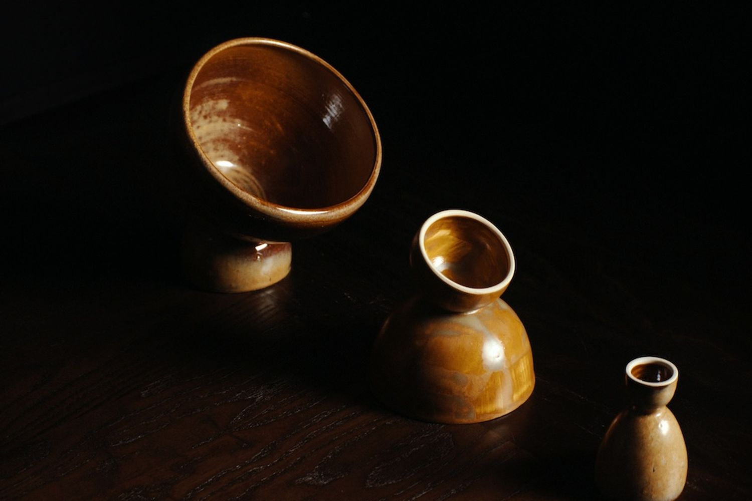 Three clay bowls of various sizes in a burnt umber colour on a dark wood table.