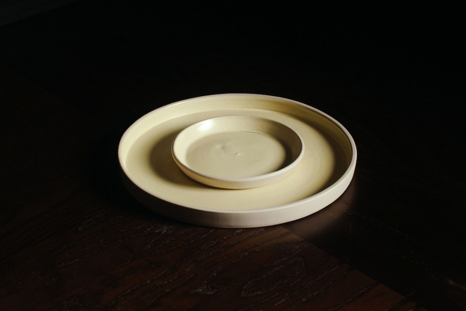 Pale yellow nested tray-style ceramic bowls on a dark wood table.