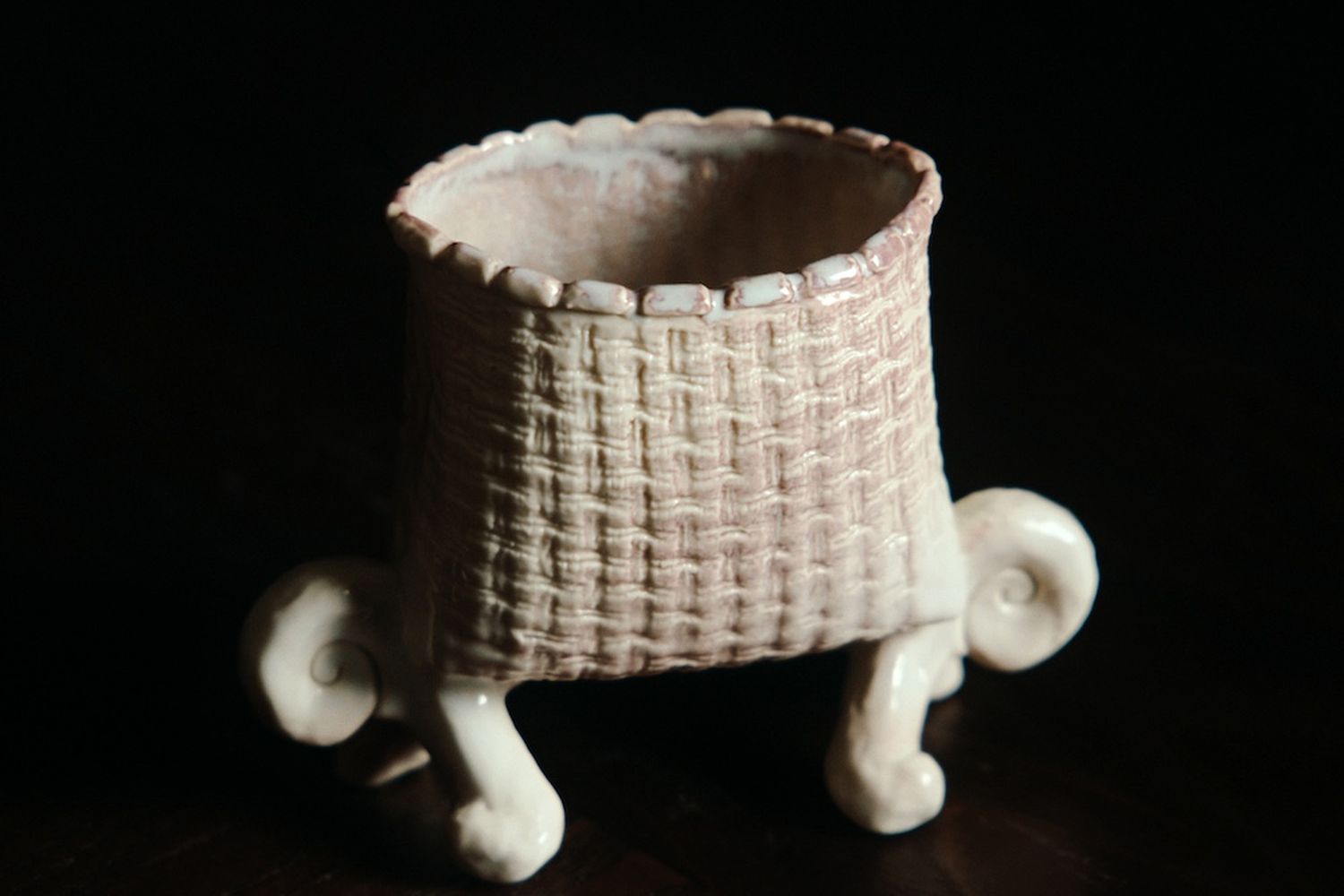 Pale pink ceramic basket with feet on a dark brown table.