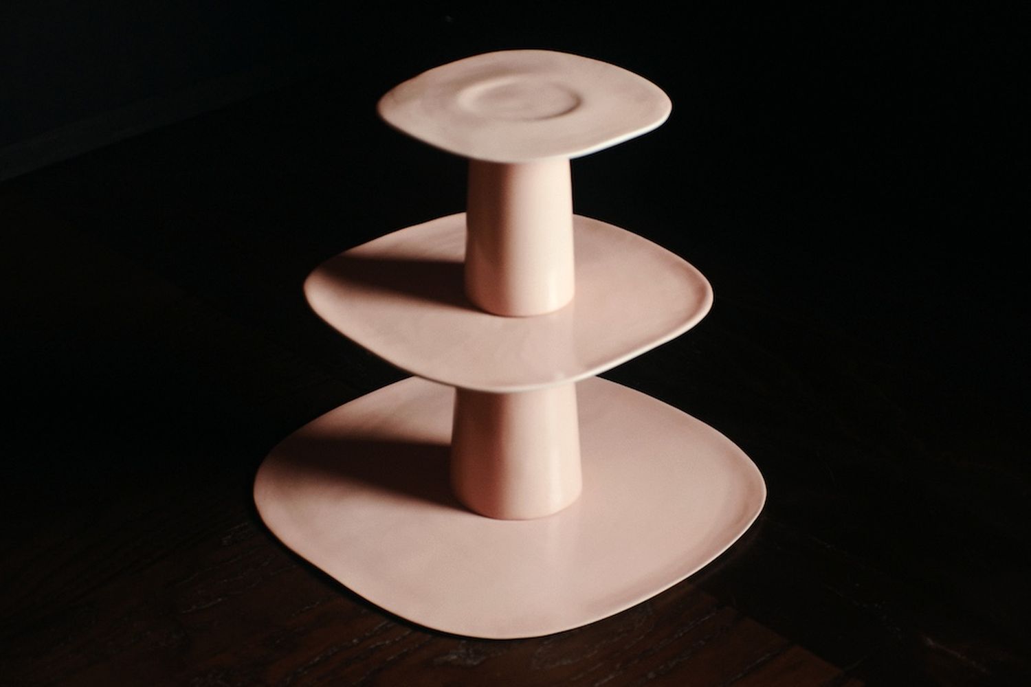 A pale pink ceramic cake stand on a dark wood table.