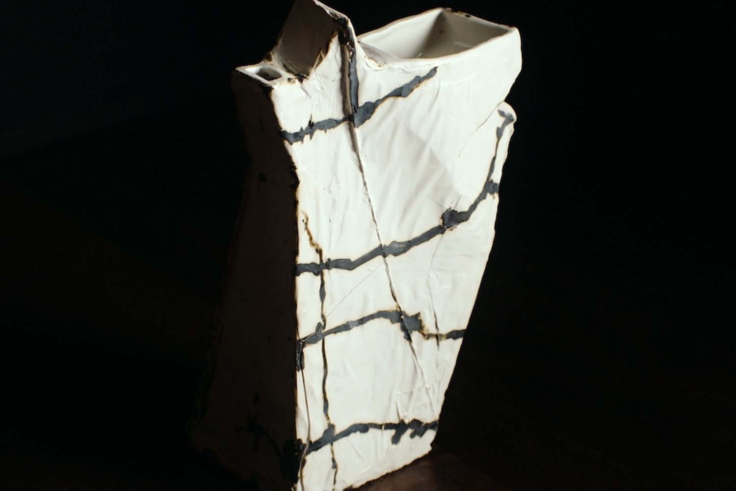 White abstract star-shaped ceramic vase on a dark wood table.