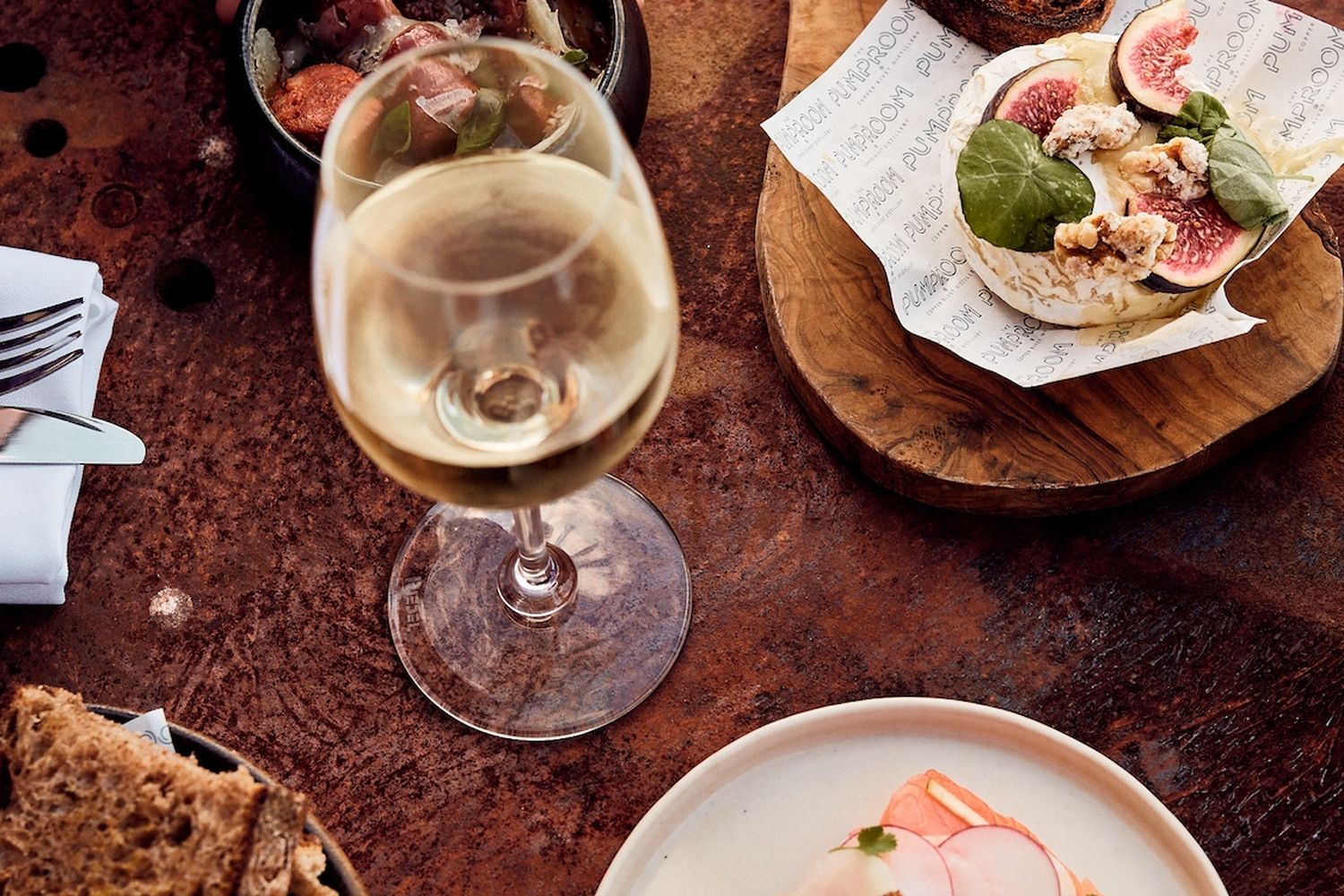 A delightful meal awaits at a charming restaurant. The table is adorned with a variety of dishes, including a delicious sandwich, a refreshing glass of white wine, and a delightful array of bread and crackers. The ambiance is enhanced by the warm glow of the candlelight and the inviting aroma of the wine. The scene is a perfect blend of comfort and indulgence. [G]