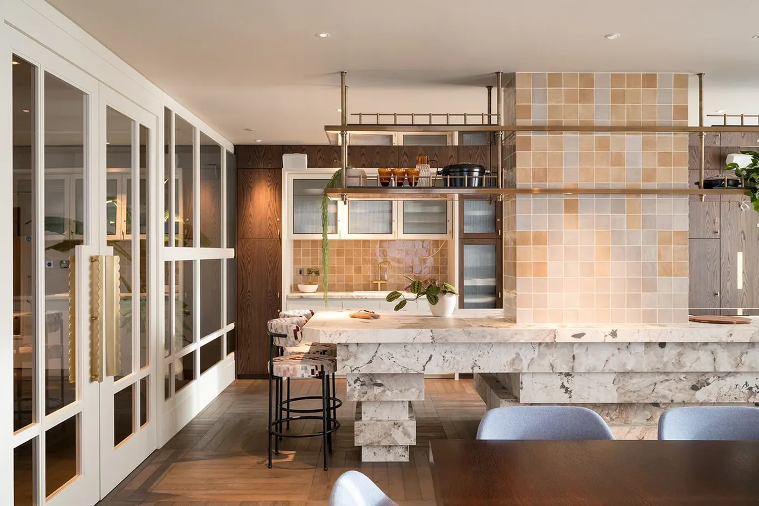 A riverstone kitchen with a white marble island, a wooden bar stool, and a potted plant. [G]