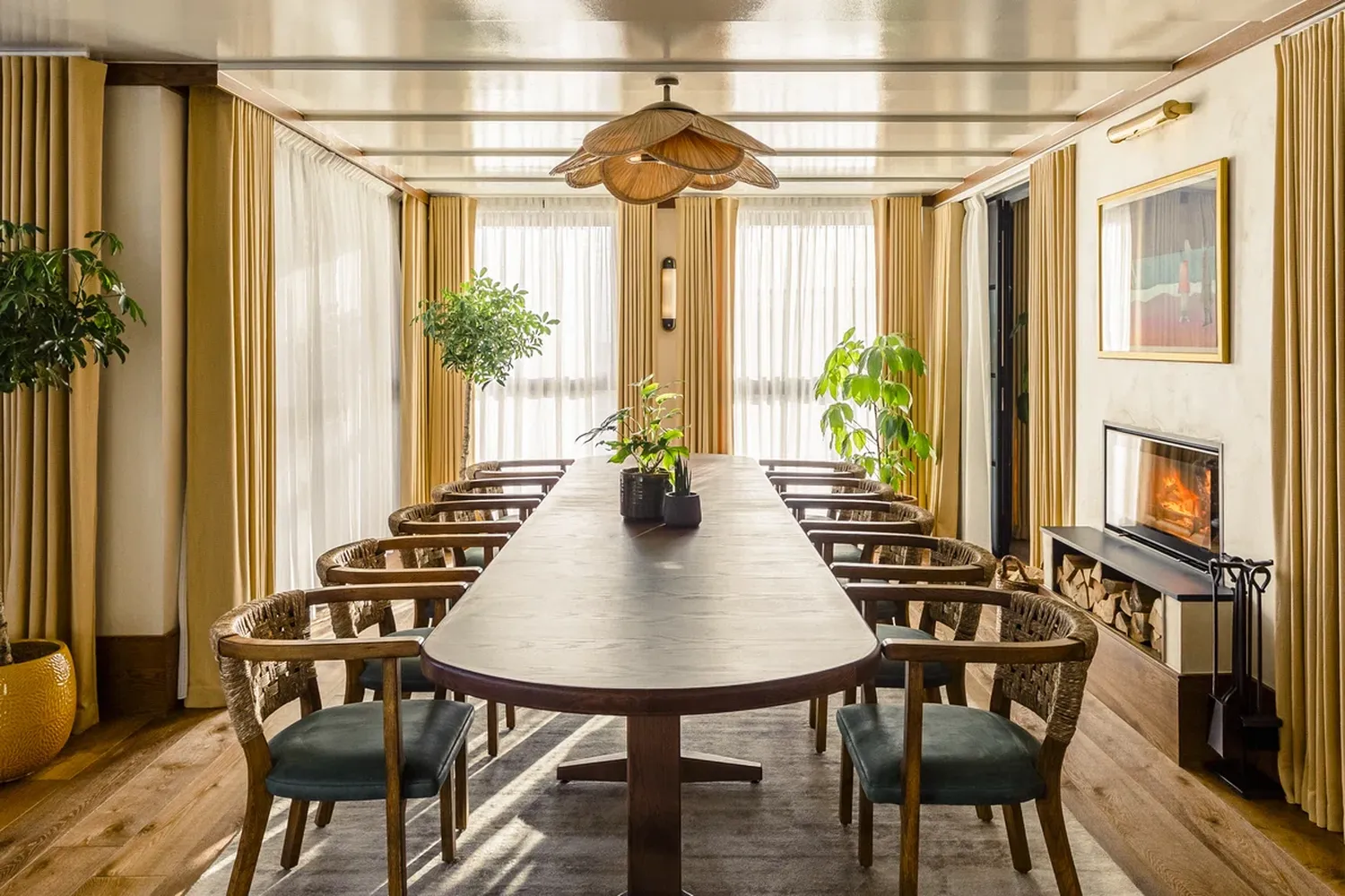 The image features a serene dining room with a wooden table and six chairs. The table is adorned with a vase of potted plants and a hanging lamp. The room is illuminated by natural light coming through a window with white curtains. The walls are painted white, and the floor is made of wood. The room exudes a warm and inviting atmosphere. [G]