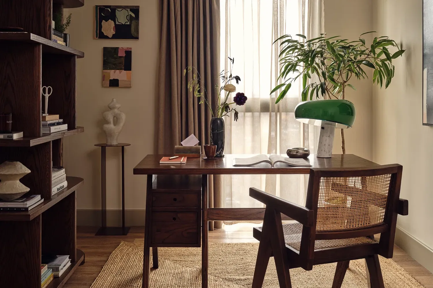The image features a serene and cozy room with a wooden desk and chair. The desk is adorned with a vase of flowers, a book, and a lamp, creating a warm and inviting atmosphere. The chair is positioned in front of the desk, ready for someone to sit and work. The room is well-lit, with natural light streaming in from a window adorned with sheer curtains. The walls are decorated with various pieces of art and photographs, adding a personal touch to the space. The overall ambiance is one of tranquility and productivity. [G]