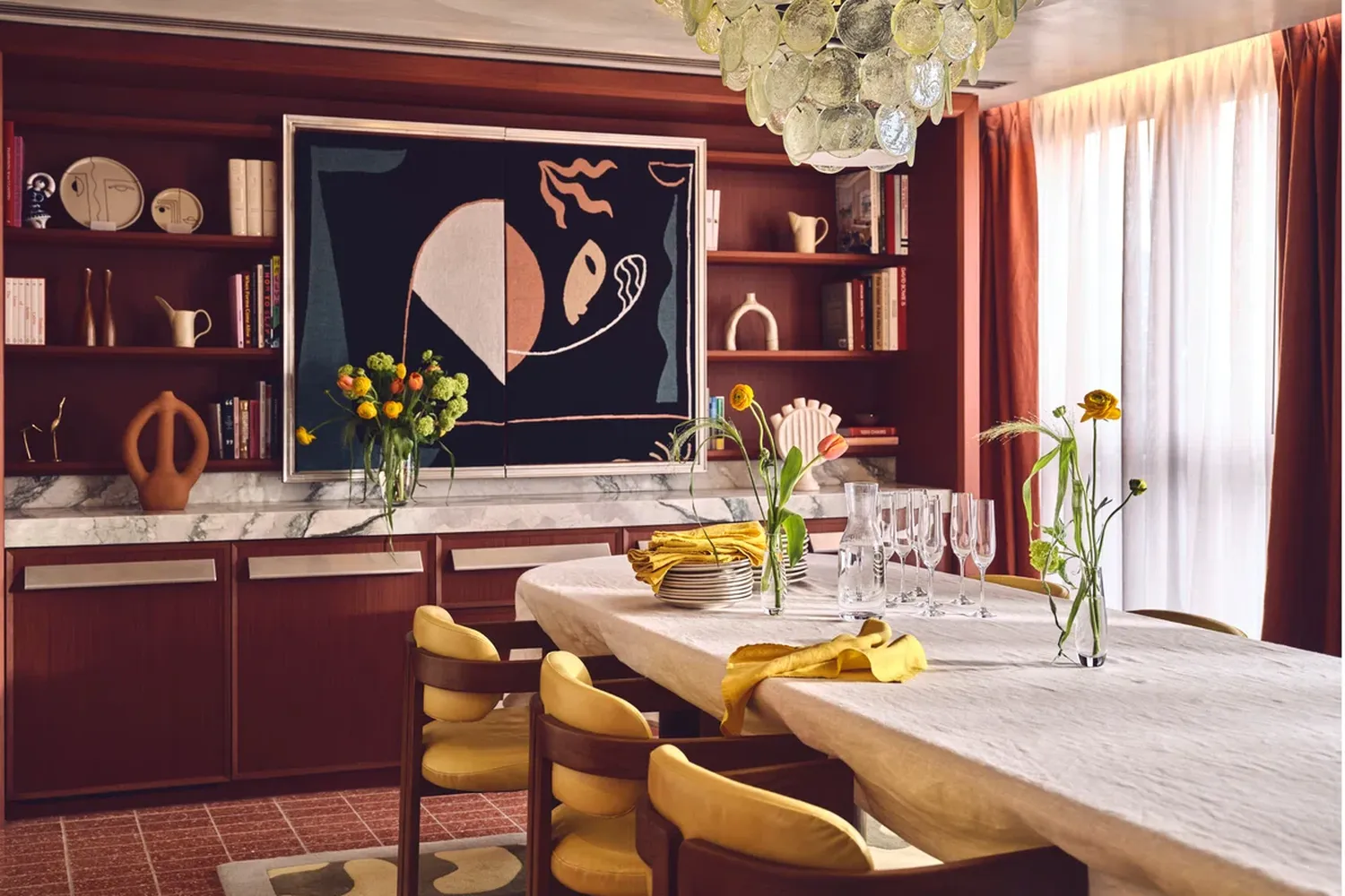 The image showcases a luxurious dining area with a sophisticated table set for four. The table is adorned with a white tablecloth and is surrounded by yellow chairs. The centerpiece of the table is a vase filled with vibrant flowers, adding a touch of freshness to the setting. The room is elegantly decorated with a large painting of a woman, a chandelier hanging from the ceiling, and a bookshelf filled with books and decorative items. The room is bathed in warm light, enhancing the overall ambiance. [G]