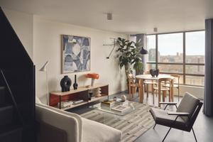 A modern living room with a glass coffee table, a white sofa, and a wooden dining table. The room has a large window overlooking a cityscape. The room features a large abstract painting, a vase, a lamp, and a plant. The room also has a rug and a rug runner. [G]