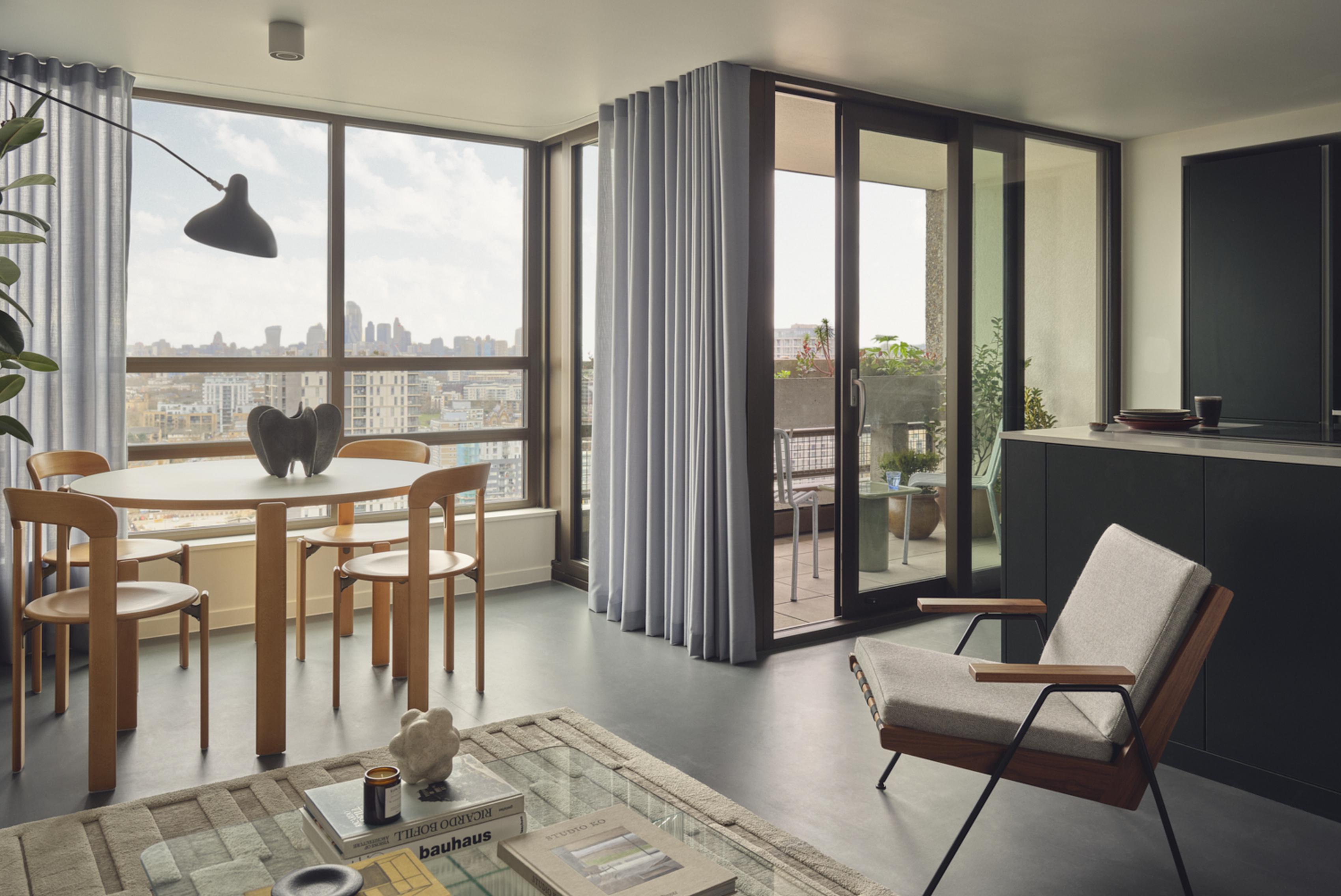 A modern living room with a large window overlooking a city skyline. The room features a modern chair, a coffee table, and a vase. The window has a large curtain, and there's a potted plant on the windowsill. The room has a minimalist aesthetic with a neutral color palette. [G]