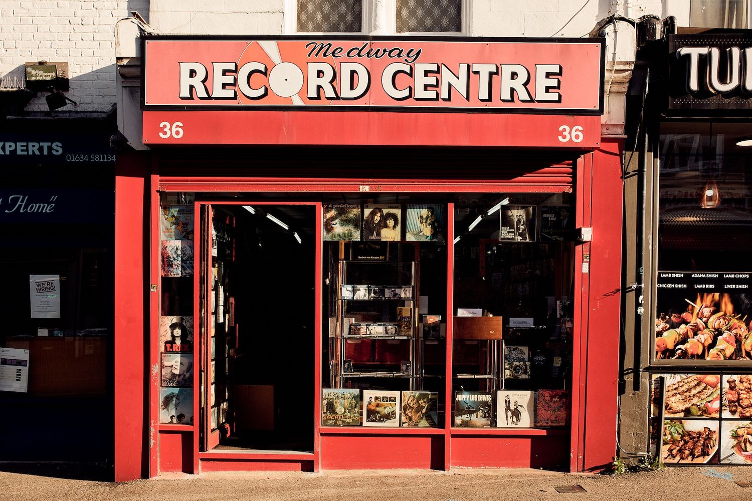The image features a red store named "The Red Gaze" with a large window displaying a variety of books and artwork. The store is located on a street with a white building in the background. The store's name is prominently displayed in white letters above the window. The number "6d40de5e76" is displayed on the window, and the store's phone number is also visible. The store appears to be a popular and well-stocked store, offering a variety of books and artwork for sale. [G]