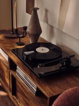 "Elegant record player on wooden console with ceramic vase, showcasing sophisticated living spaces at Way of Life luxury apartment rentals." [G]