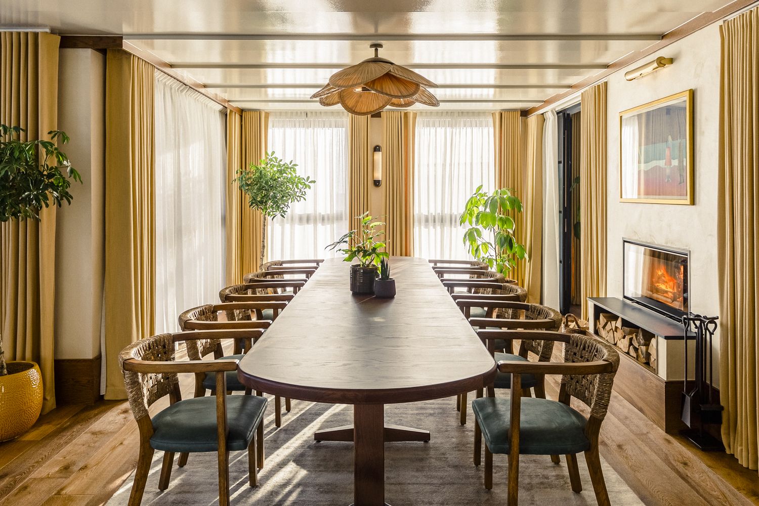 A cozy dining room with a wooden table, green chairs, and a potted plant. The room has white walls, a wooden floor, and a window with yellow curtains. A hanging lamp with a bamboo shade hangs from the ceiling. [G]