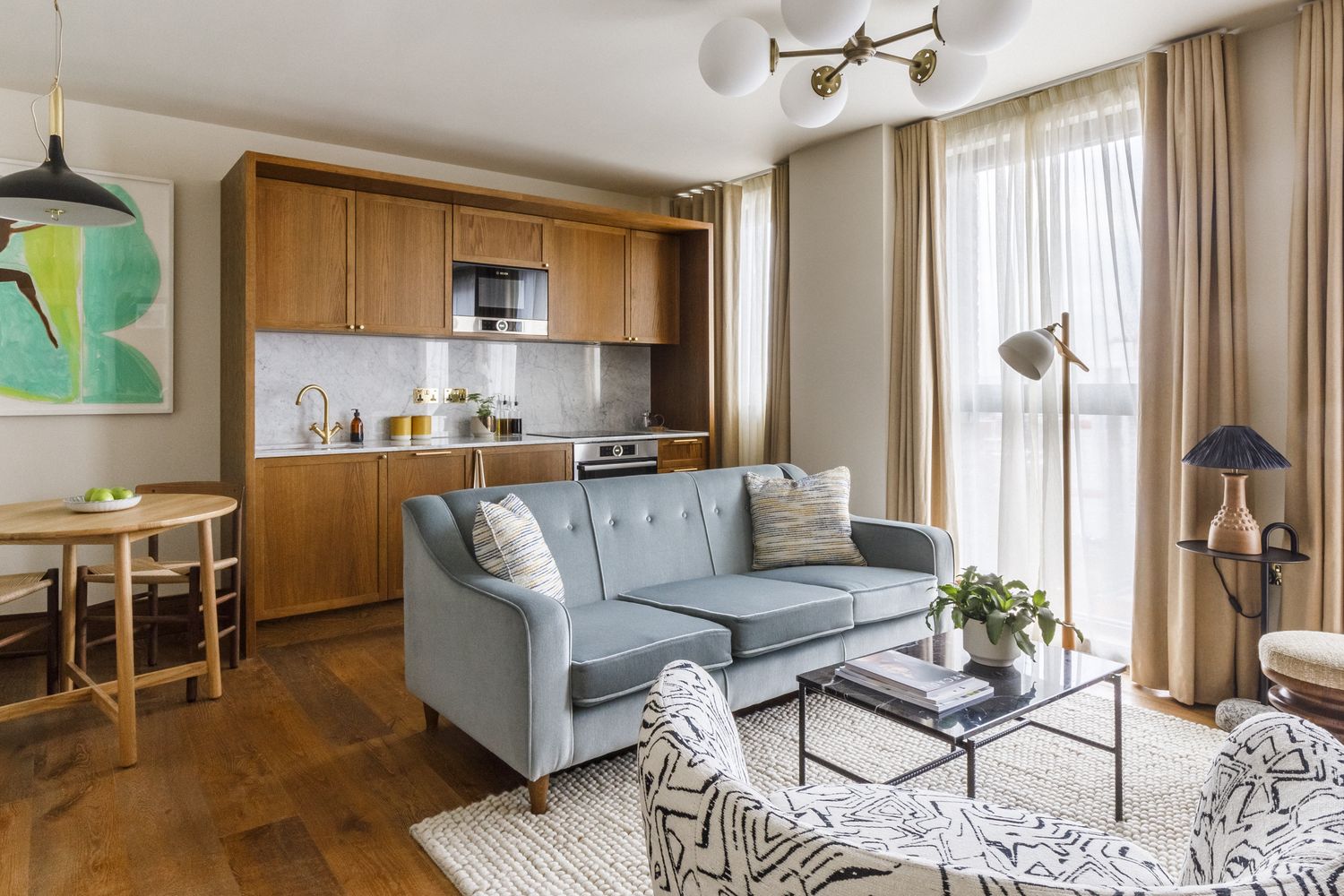 A modern living room with a blue sofa, a zebra print armchair, and a coffee table. The room has wooden cabinets, a black microwave, and a chandelier. The floor is covered with a rug. [G]