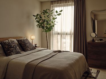 "Elegant bedroom with potted plant, natural light, and modern furnishings in Way of Life luxury apartments to rent." [G]