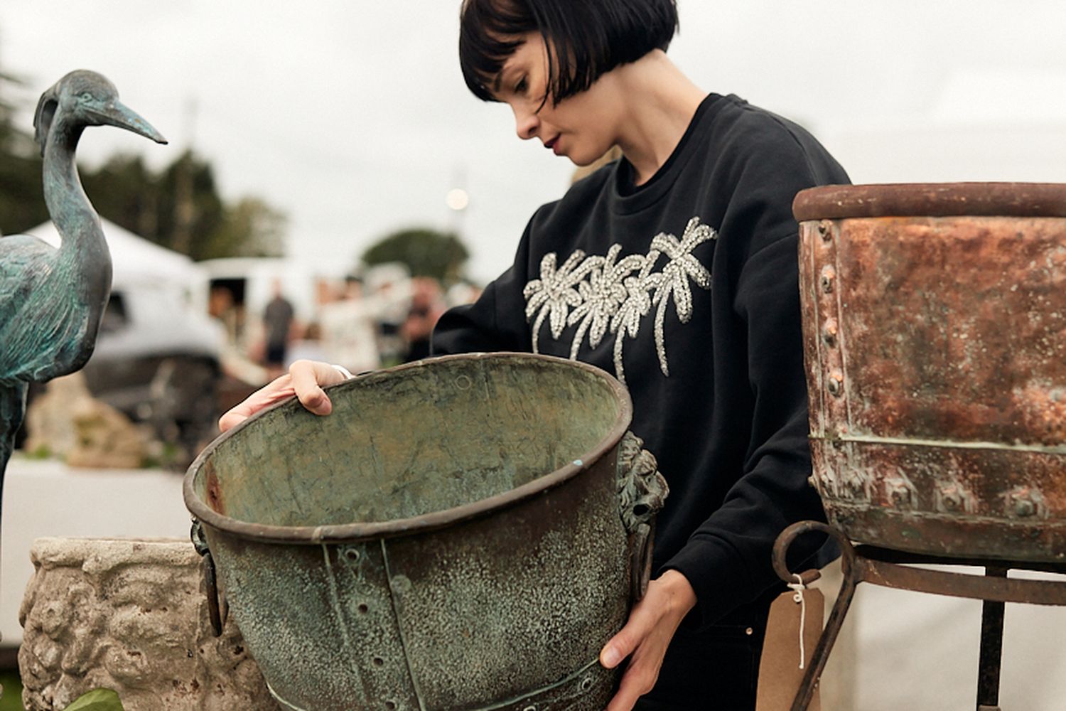 A woman looks at an aged metal pot.