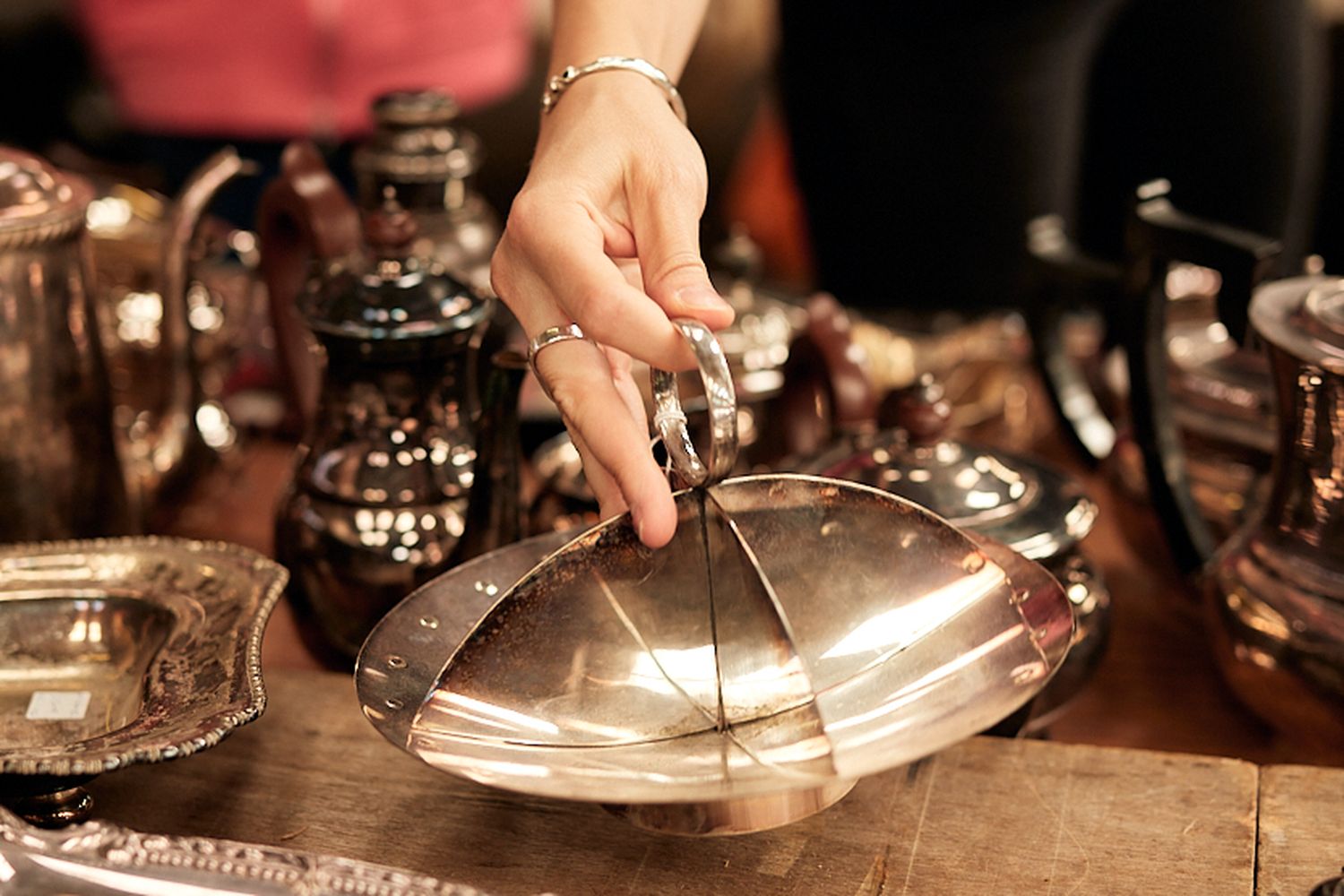 A woman is holding a silver dish over a wooden table.