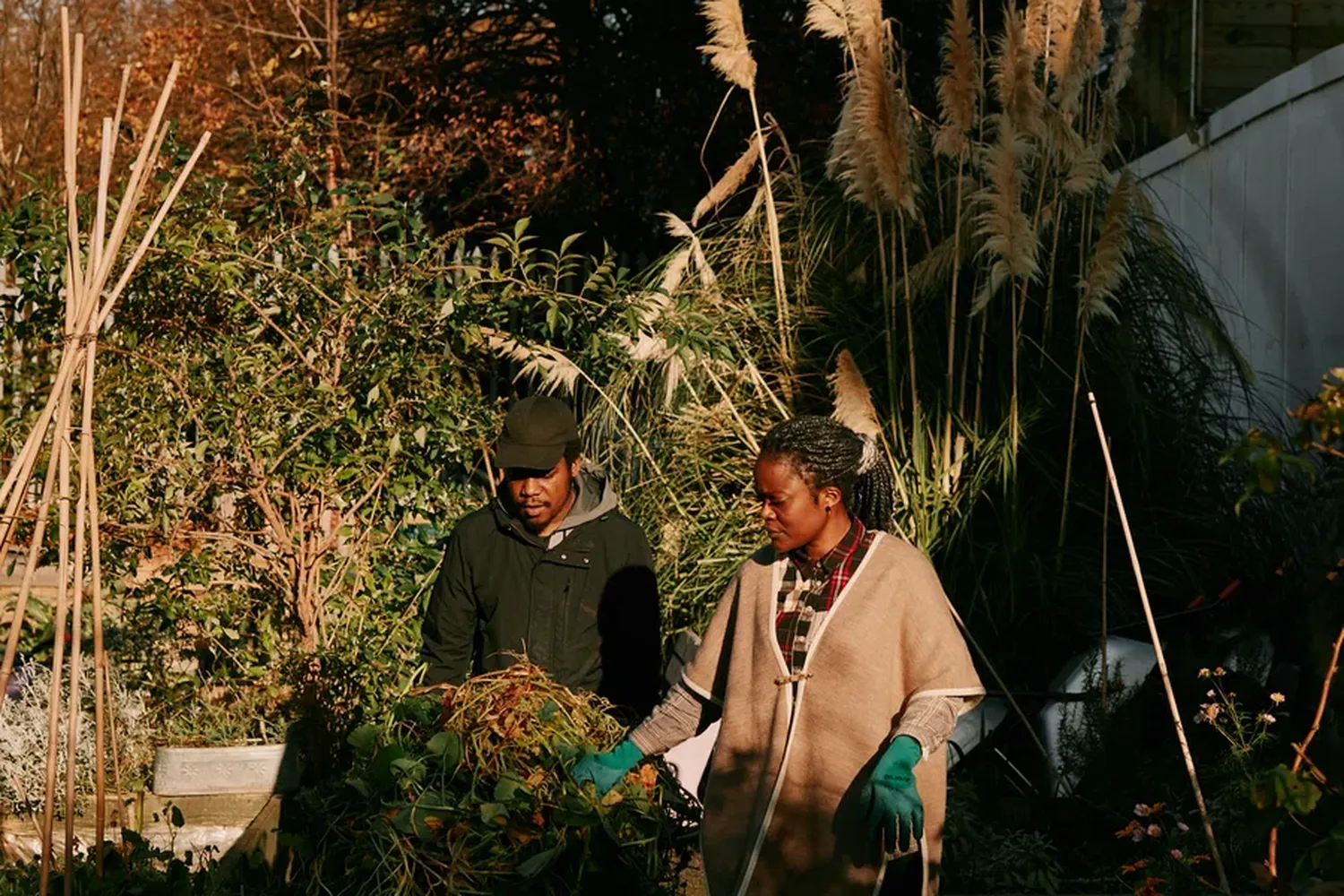 A woman in a green coat and a man in a black coat are working in a garden. [G]