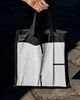 A person holding a balck tote bag with a large 'K' logo in white