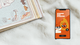 Smartphone on a soft surface displaying a streak tracker app with animated characters. A book with a map is partially visible beside it.