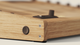 Close-up of a wooden electronic music instrument featuring buttons and a control knob, set against a light background.