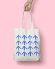 A hand holding a white totebag with a pattern of repeating blue arrows, pointing upwards