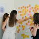 Three people in a workshop putting post its on a wall