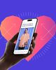 A hand holding a phone, in a cut out of a pink heart