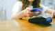 A person holding a mobile phone over a wireless payment terminal and a cafe