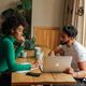 Two people collaborating, sitting across from one another at a wooden table and looking at a laptop
