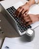 A close up of a person using a mac laptop, with a small gray and white device next to the computer