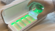 Gloved hand holding a glowing item over a case with illuminated slots, inside a sterile-looking environment.