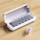 Open white weekly pill organizer on a wooden surface, with removable compartments labeled Mon-Sun. One compartment is placed outside the case.