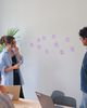 People in a meeting room discussing ideas with sticky notes on the wall. Laptops are on the table, and a plant is in the background.